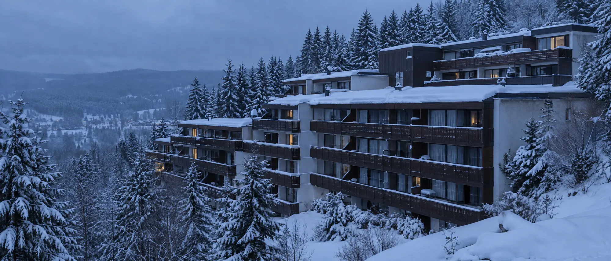 Verschneite Ferienwohnanlage aus den 70er-Jahren an einem Fichtenhang im Oberharz, die meisten Fenster dunkel